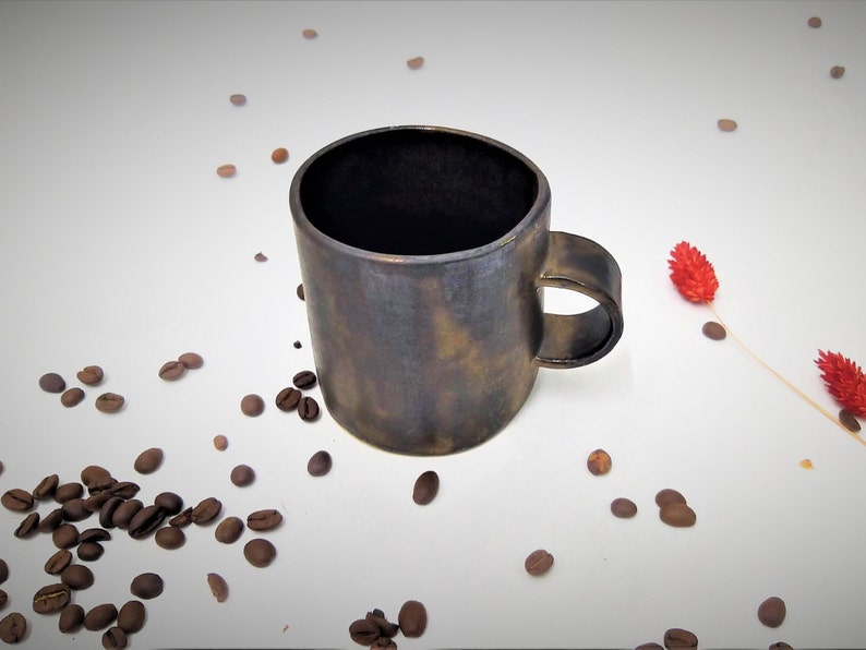 May include: A dark brown ceramic coffee mug with a textured, speckled finish. The mug has a rounded handle and a wide, slightly flared rim.