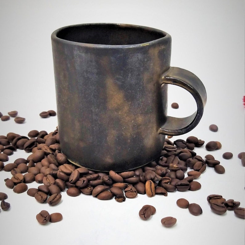 May include: A dark brown ceramic mug with a textured, speckled finish. The mug has a rounded handle and is surrounded by coffee beans.