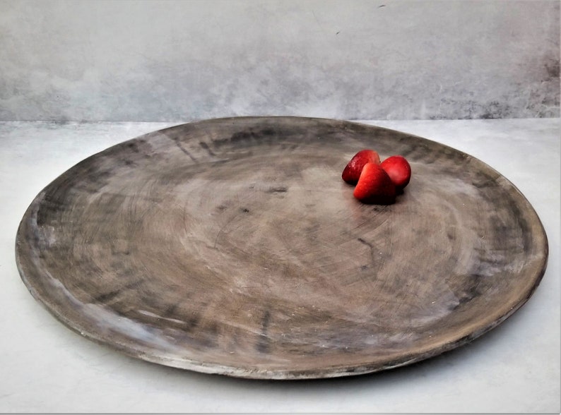 May include: A large, round, gray ceramic serving platter with three red strawberries on top.
