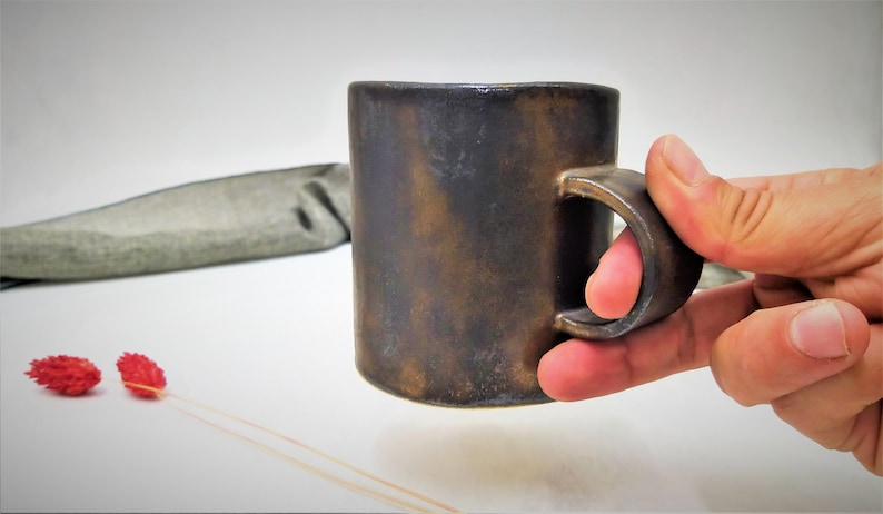 May include: A dark brown ceramic mug with a rounded handle. The mug has a rustic, aged look.