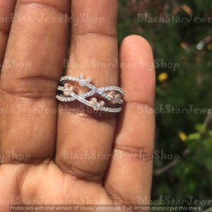 May include: A silver and rose gold ring with a delicate design featuring a series of intertwined bands and small, sparkling cubic zirconia stones. The ring is adorned with a Mickey Mouse silhouette in the center.