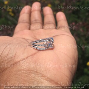 May include: A silver ring with three bands and small clear stones. The ring has a larger pink stone in the center.