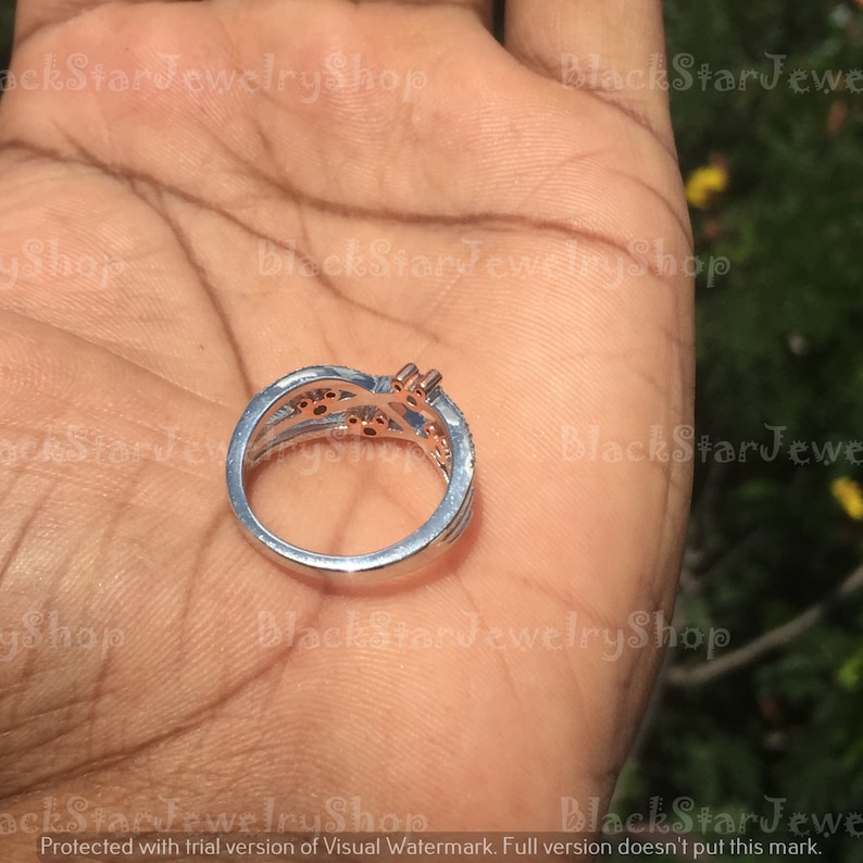 May include: A silver ring with a delicate design featuring multiple bands and small, clear stones. The ring has a rose gold accent on the band.