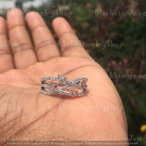 May include: A silver and rose gold ring with a delicate design featuring intertwined bands and small clear and pink stones. The ring has a Mickey Mouse silhouette in the center.