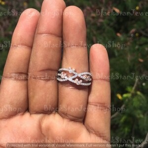 May include: A silver and rose gold ring with a criss-cross design and small clear and pink stones.