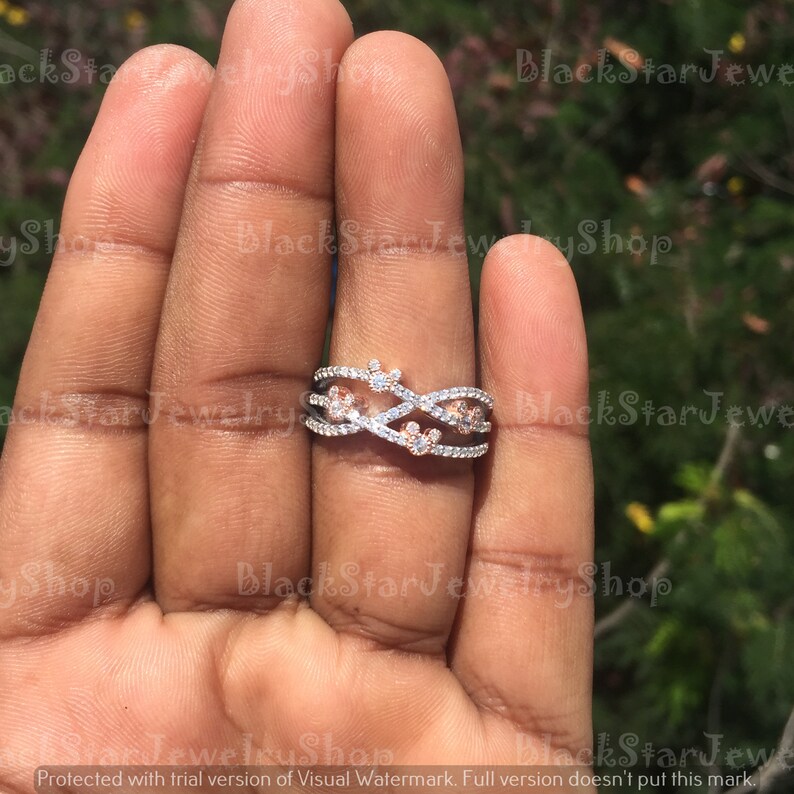May include: A silver and rose gold ring with a criss-cross design and small clear and pink stones.