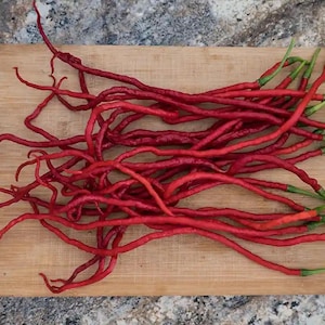 May include: A bunch of long, thin, red chili peppers with green stems on a wooden cutting board.
