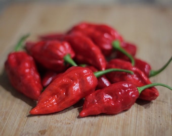 May include: A close-up of a pile of bright red chili peppers on a wooden surface. The peppers are all pointed and have a glossy finish.