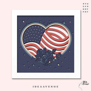 May include: A layered paper art piece featuring a heart-shaped design with the American flag and blue roses. The artwork is set against a dark blue background with star cutouts and is framed in white. The text "IDEA AVENUE" is at the bottom.