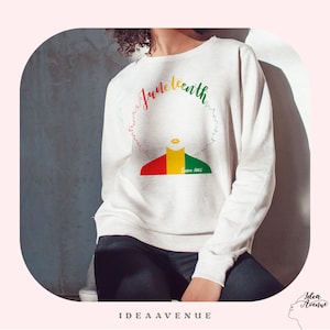 Puede incluir: Sudadera blanca con un diseño gráfico de un rostro estilizado de una mujer negra con un peinado afro. El texto "Juneteenth" está escrito en una fuente cursiva colorida alrededor de la cabeza de la mujer. El texto "Since 1865" está escrito debajo del rostro de la mujer.