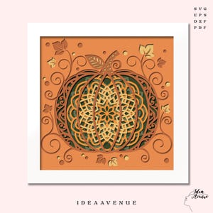 May include: A layered paper art piece featuring a pumpkin design in shades of orange, green, and tan. The pumpkin has intricate cut-out details and is surrounded by decorative leaves and vines. The text "IDEA AVENUE" is at the bottom.