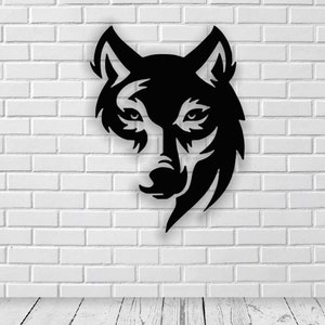 Op de afbeelding: Zwarte silhouet van een wolfskop met een gestileerd ontwerp. De wolfskop is naar voren gericht met de mond gesloten. De achtergrond is een witte bakstenen muur.