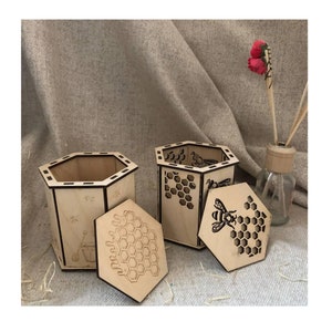 May include: Two wooden hexagonal boxes with intricate honeycomb designs and bee illustrations. The boxes are open and the lids are placed next to them.
