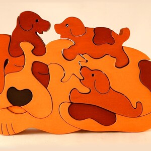 May include: A wooden puzzle of three orange and brown dogs, with the largest dog lying down and the two smaller dogs sitting on top of it.