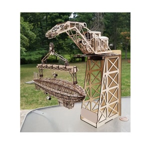 May include: A wooden model of a crane lifting a wooden model of an airship. The crane is made of laser-cut wood and has a detailed design. The airship is also made of laser-cut wood and has a detailed design.