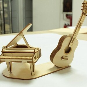 Op de afbeelding: Een houten model van een vleugelpiano en een akoestische gitaar. De piano heeft een opgetild deksel en de gitaar heeft een gedetailleerd toetsbord.