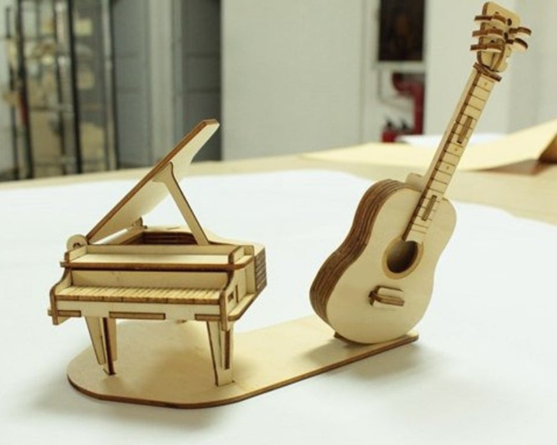 Op de afbeelding: Een houten model van een vleugelpiano en een akoestische gitaar. De piano heeft een opgetild deksel en de gitaar heeft een gedetailleerd toetsbord.