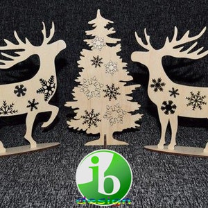 Può includere: Tre decorazioni natalizie in legno: un albero di Natale e due renne. L'albero e le renne sono decorate con fiocchi di neve neri.