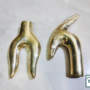 May include: Two gold-colored metal decorative handles. One handle is shaped like a stylized bird's head with a curved neck. The other handle is shaped like a pair of hands with the fingers curled inward.