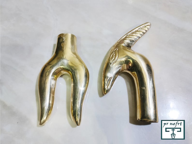 May include: Two gold-colored metal decorative handles. One handle is shaped like a stylized bird's head with a curved neck. The other handle is shaped like a pair of hands with the fingers curled inward.