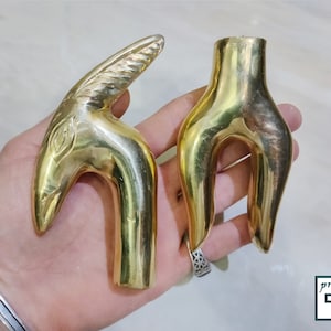 May include: Two gold-colored metal cane handles. One handle is shaped like a bird's head with a detailed design. The other handle is a simple, curved shape.