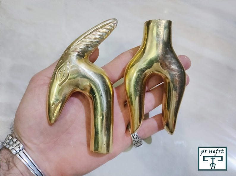 May include: Two gold-colored metal cane handles. One handle is shaped like a bird's head with a detailed design. The other handle is a simple, curved shape.