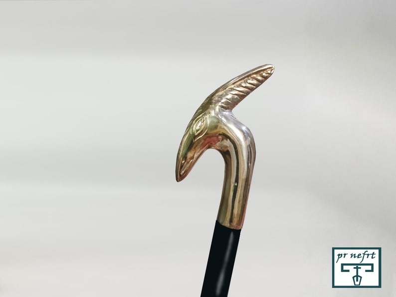 May include: A gold-colored walking stick with a decorative animal head handle. The handle is shaped like a bird's head with a long, curved beak.