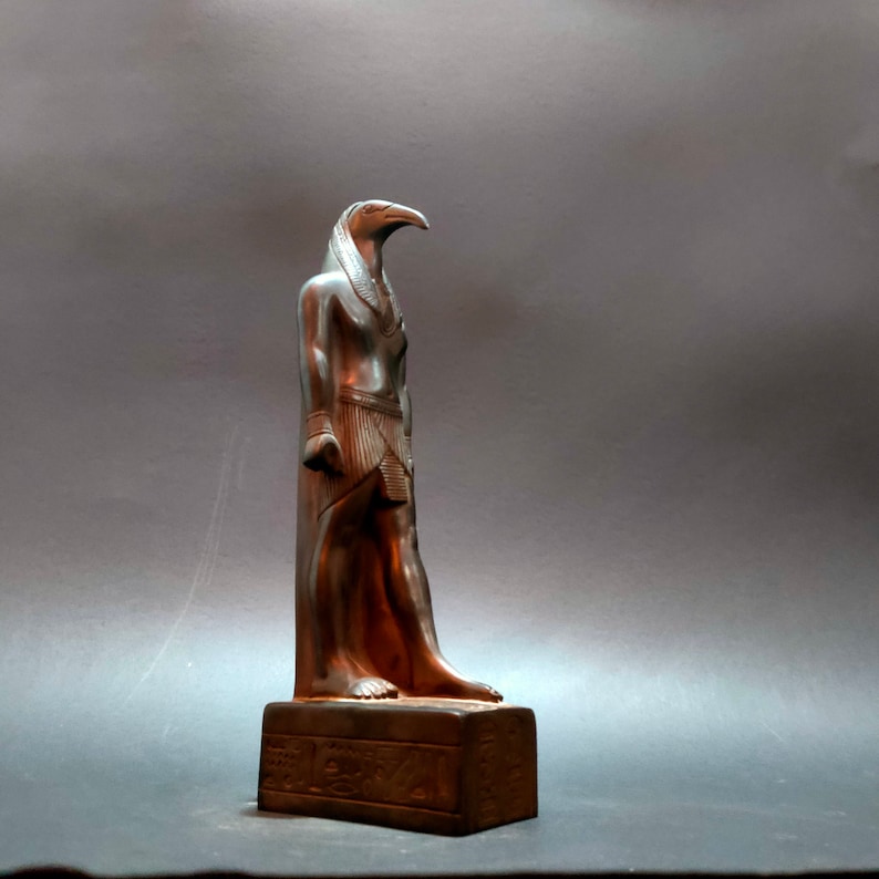 May include: A silver statue of the Egyptian god Horus, depicted as a falcon-headed man, standing on a base with hieroglyphics.