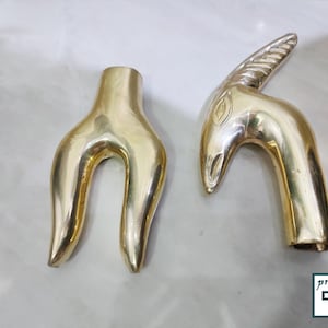 May include: Two gold-colored metal decorative handles. One handle is shaped like a stylized human hand with two fingers extended. The other handle is shaped like an animal head with a horn.