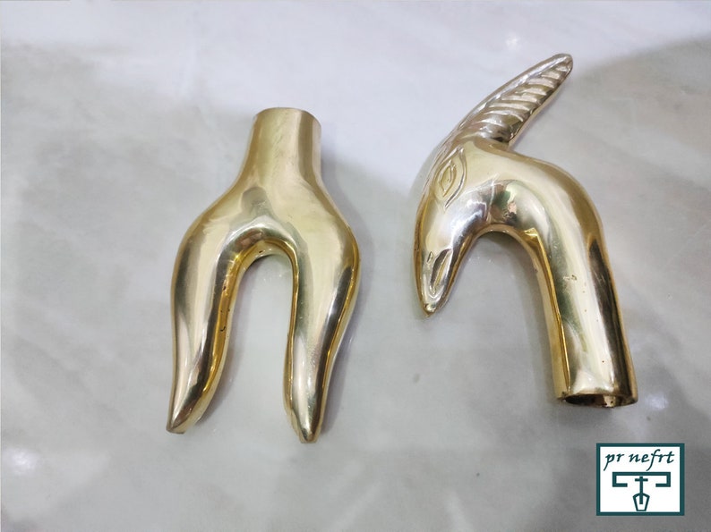 May include: Two gold-colored metal decorative handles. One handle is shaped like a stylized human hand with two fingers extended. The other handle is shaped like an animal head with a horn.