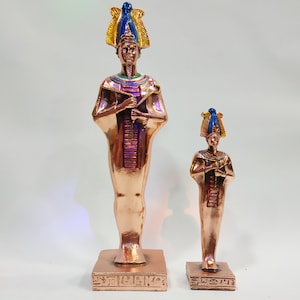 Puede incluir: Dos estatuas doradas de faraones egipcios con tocados coloridos y detalles intrincados. Las estatuas están de pie sobre bases cuadradas con inscripciones jeroglíficas.