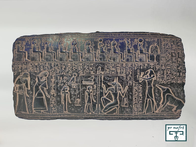 May include: A black stone relief depicting an ancient Egyptian scene. The relief shows a procession of figures, including a seated god with a jackal head, a scale, and a man holding a staff. Hieroglyphic text is inscribed around the figures.