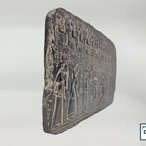 May include: A black stone relief with hieroglyphics and figures of people. The relief is carved with intricate details and depicts a scene from ancient Egyptian history.