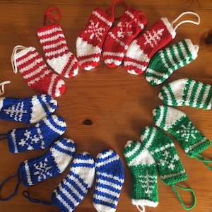 May include: A selection of miniature knitted Christmas stockings in red, white, blue, and green. Some have snowflake or striped patterns. Each stocking has a loop for hanging, ideal for festive decorations.