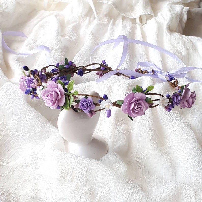 May include: A purple and white flower crown with a satin ribbon. The crown is made of artificial flowers and is perfect for a wedding or other special occasion.