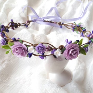 May include: A purple and white flower crown with a lavender ribbon. The crown is made of faux flowers and vines.