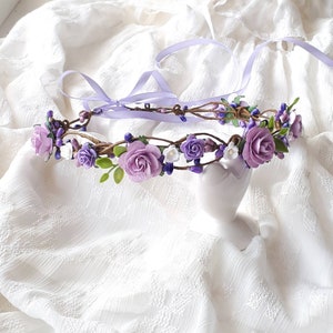 May include: A purple and white flower crown made of artificial flowers and vines. The crown is on a white fabric background.