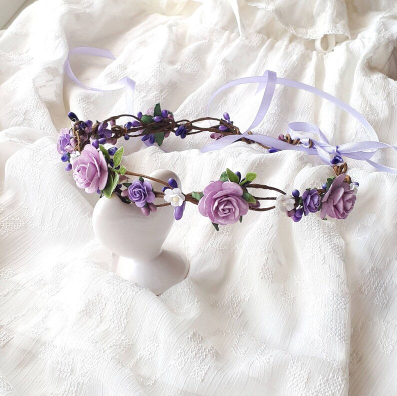 May include: A purple and white flower crown with a delicate floral design. The crown is made with artificial flowers and is perfect for a special occasion.