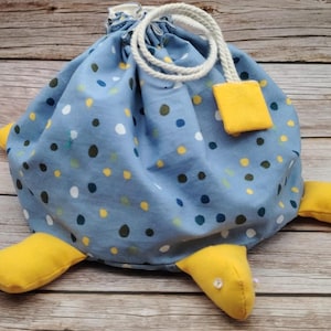 Peut inclure: Un sac bleu à cordon de serrage avec un motif de tortue. Le sac est décoré de pois colorés et possède des pieds de tortue jaunes. Une corde blanche et un accent carré jaune complètent le design.