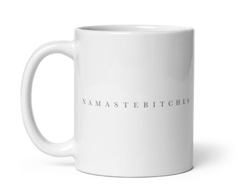 Puede incluir: Taza de café de cerámica blanca con el texto "NAMASTEBITCHES" impreso en gris en la parte delantera.