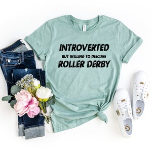 May include: A light blue t-shirt with the text "Introverted but willing to discuss roller derby" in black.