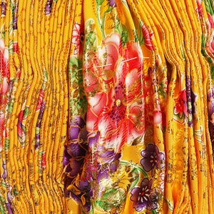 May include: Yellow fabric with a pleated texture and a floral pattern in shades of red, purple, green, and gold.