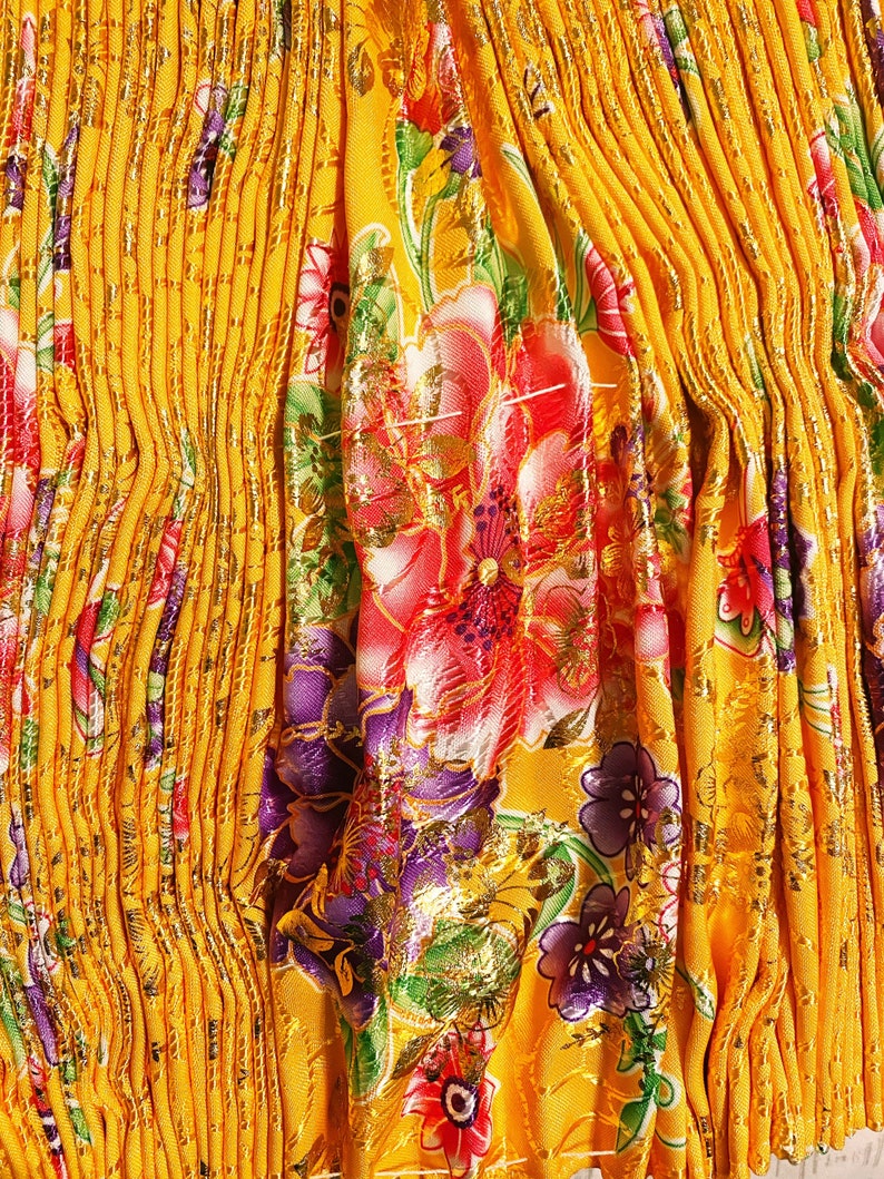 May include: Yellow fabric with a pleated texture and a floral pattern in shades of red, purple, green, and gold.