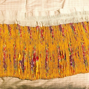 May include: A yellow fabric with a floral pattern is pleated and gathered at the top. The fabric is white at the top and has a ruffled edge.