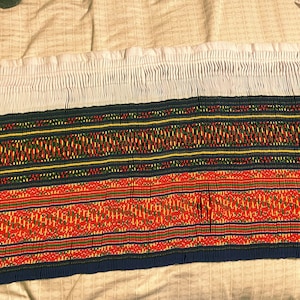 May include: A white fabric with a ruffled edge, followed by a band of blue, red, yellow, and green woven fabric with a geometric pattern.