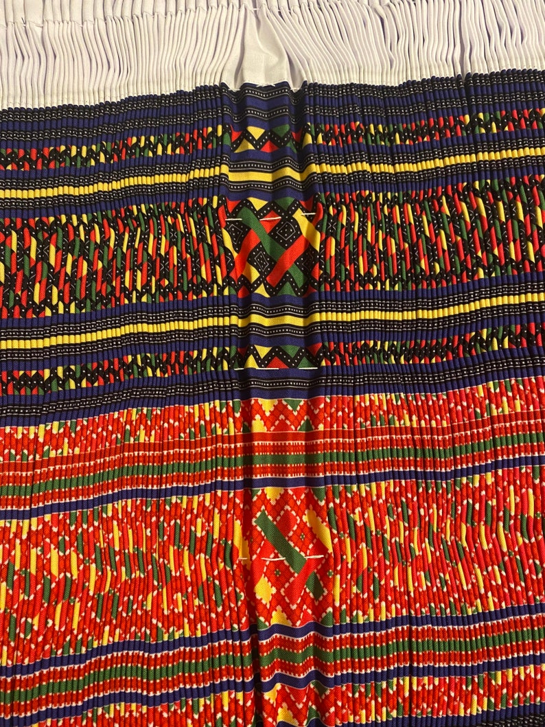 May include: A close-up of a colorful fabric with a repeating geometric pattern. The fabric is made up of red, yellow, green, blue, and black threads. The pattern is symmetrical and intricate.