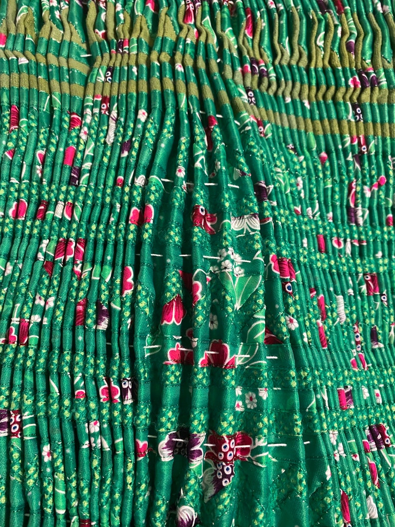 May include: Green fabric with a floral pattern and pleats. The fabric is gathered and sewn together to create a ruffled look.