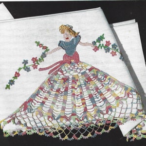 May include: Embroidered white handkerchief featuring a woman in a dress holding floral garlands. The dress is a colorful patchwork design with a scalloped lace hem. The woman's top is blue, and her hair is blonde.