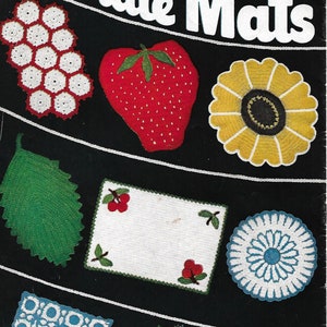 May include: A vintage crochet pattern book cover featuring a variety of crocheted hot plate mats, including a strawberry, a sunflower, a leaf, a cherry design, a geometric design, and a daisy design. The cover is black with white text that reads "Hot Plate Mats" and "Star Book No. 70".