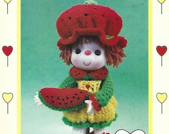 May include: Crochet doll pattern for a watermelon slice doll. The doll is wearing a red and green outfit and holding a watermelon slice. The pattern is by Dumplin Designs.